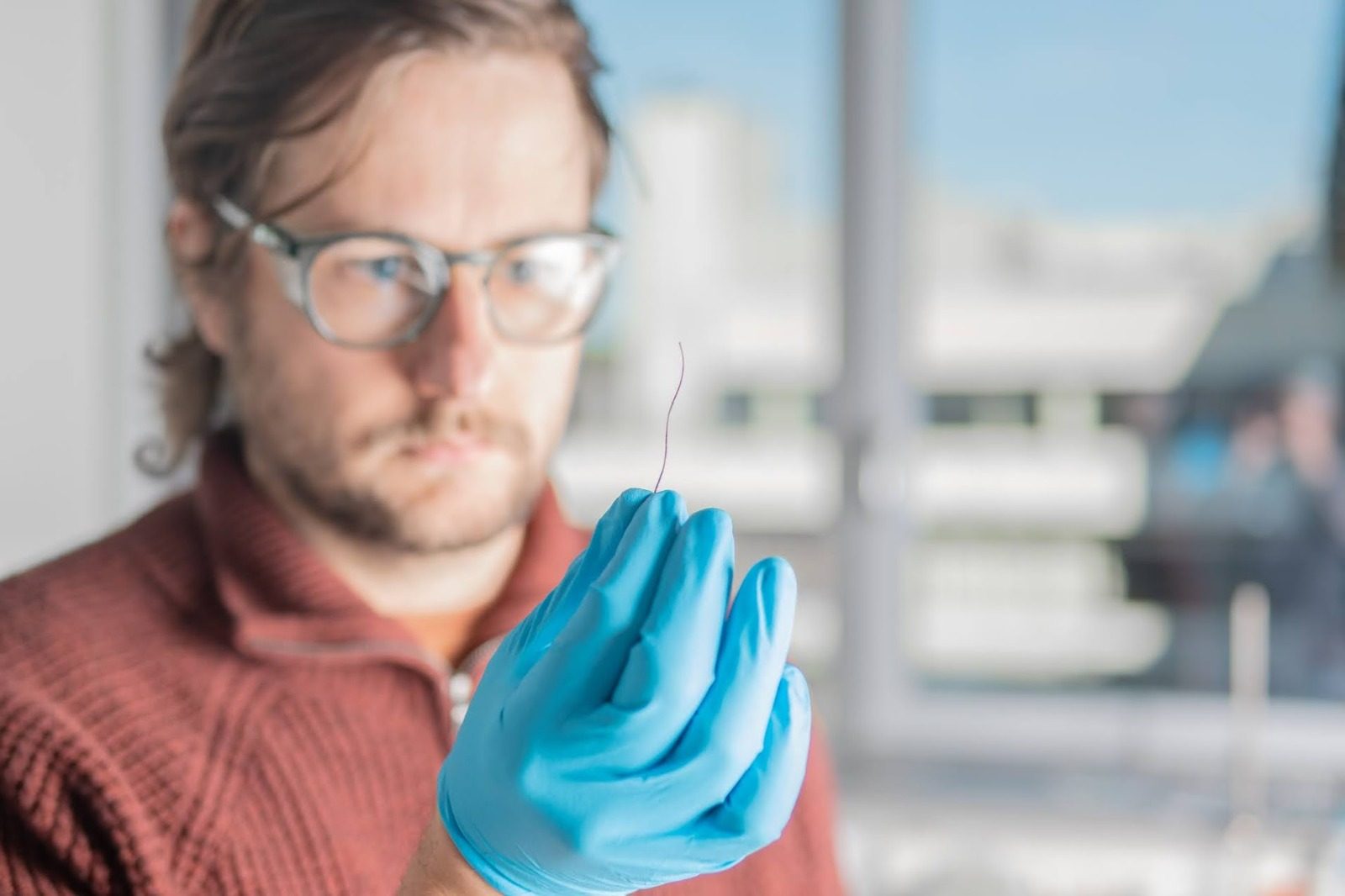 A researcher in blue lab gloves holds up a single elephant whisker between his fingertips