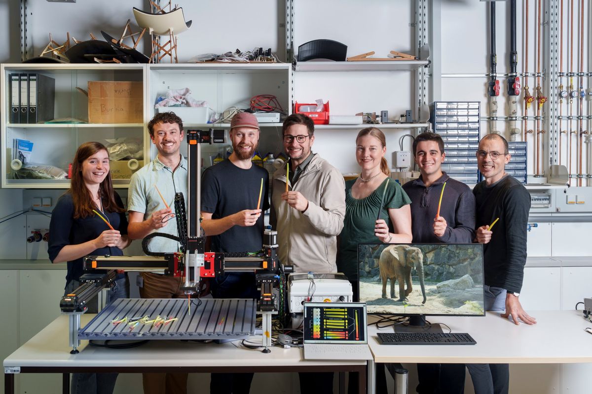 The team holding 3D-printed graded whiskers beside the multimaterial printer