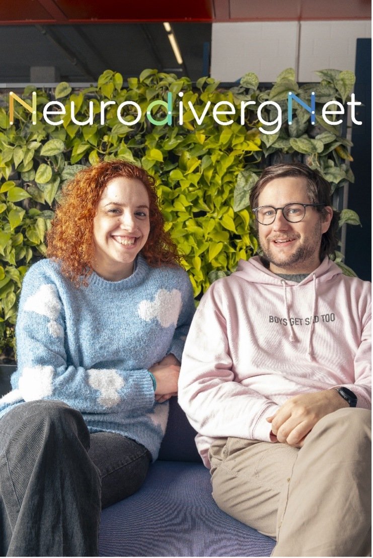 Two NeurodivergNet co-founders smiling on a sofa in front of a green plant wall, with the NeurodivergNet logo above them